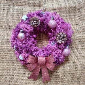 Puede incluir: Una corona de Navidad rosa y blanca hecha de musgo con adornos rosas y un lazo de purpurina rosa.