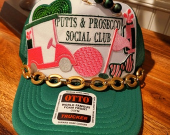 Putts and Prosecco Social Club Trucker hat with golf themed patches in pink and green.