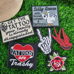 May include: Collection of embroidered patches with various designs. Includes patches with text like "Get the Tattoo" and "Tattoos are Trashy." Other patches feature a goose, a skeleton hand, a red swallow, and a rose.