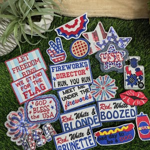 May include: A collection of patriotic patches in red, white, and blue. Designs include stars, flags, and text like "Let Freedom Ring" and "God Bless the USA." Some patches feature sequins and glitter.