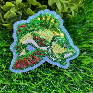 May include: A decorative fish-shaped patch with a light blue border. The fish features green and gold sequins on its back, red accents on its fins, and white details. This patch is suitable for adding to clothing or accessories.