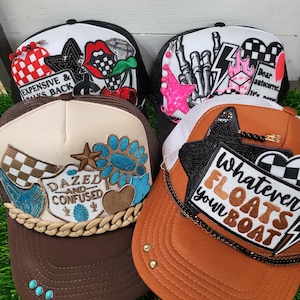 May include: Four trucker hats with various designs. One hat has the text "EXPENSIVE & ALWAYS BACK" with a red and white checkered pattern. Another has a pink star and the text "Dear autocorrect, It's never". The other two hats have the text "DAZED AND CONFUSED" and "Whatever FLOATS your BOAT".