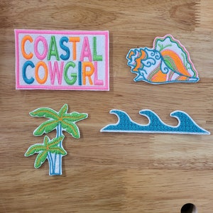 May include: Four embroidered iron-on patches with a coastal theme. The patches feature a seashell, palm trees, waves, and the text "COASTAL COWGIRL".