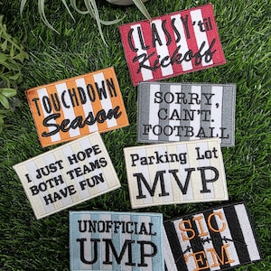 May include: A collection of seven rectangular embroidered patches with striped backgrounds and black or orange text. The patches feature phrases including CLASSY 'til Kickoff, TOUCHDOWN Season, SORRY, CAN'T. FOOTBALL, I JUST HOPE BOTH TEAMS HAVE FUN, Parking Lot MVP, UNOFFICIAL UMP, and SIC 'EM.