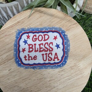 Pu&ograve; includere: Toppa rettangolare con la scritta "GOD BLESS the USA" ricamata in rosso e bianco su sfondo blu. La toppa ha un bordo sfilacciato ed &egrave; decorata con stelle rosse e blu.