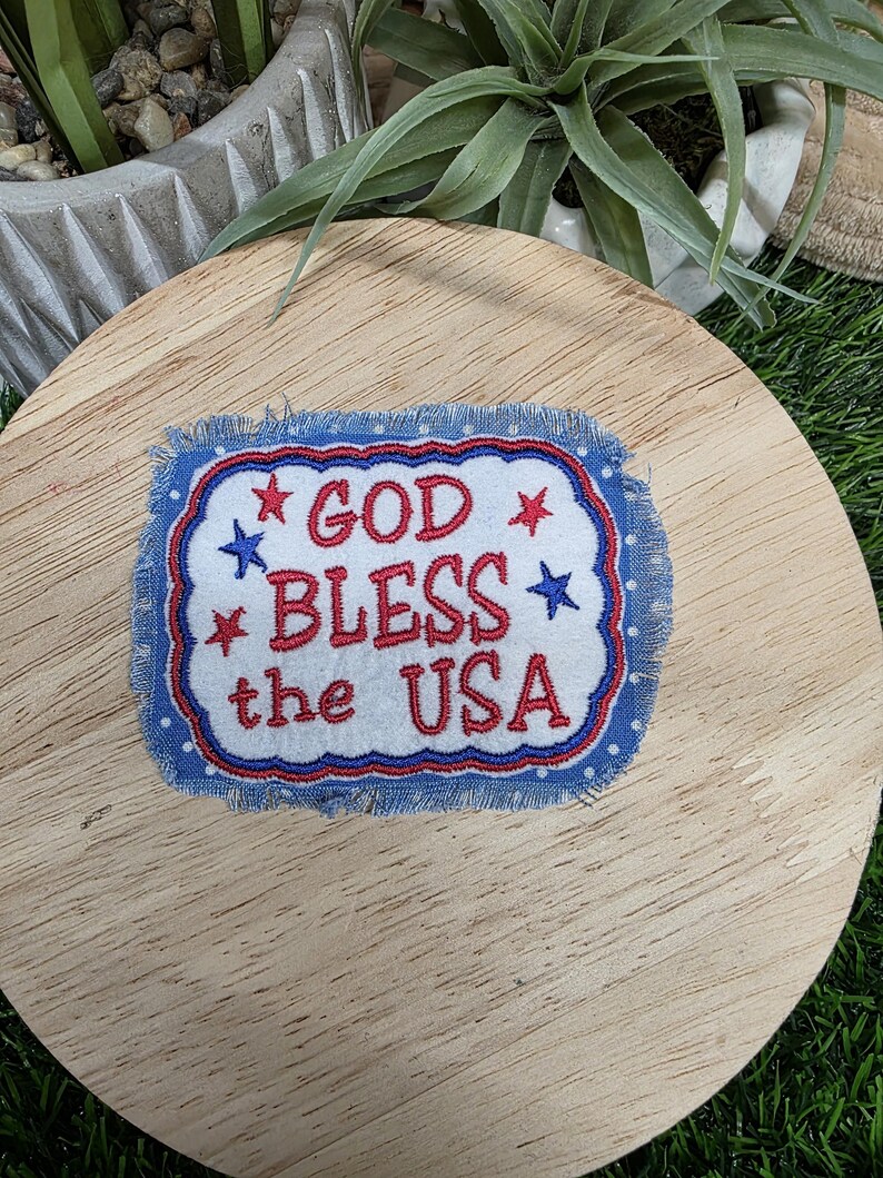 Pu&ograve; includere: Toppa rettangolare con la scritta "GOD BLESS the USA" ricamata in rosso e bianco su sfondo blu. La toppa ha un bordo sfilacciato ed &egrave; decorata con stelle rosse e blu.