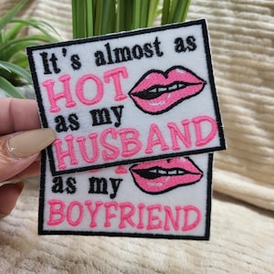 May include: Two white embroidered patches with black borders. The top patch reads "It's almost as HOT as my HUSBAND" in pink lettering, with a pink lip graphic. The bottom patch reads "as my BOYFRIEND" in pink lettering, with a pink lip graphic.
