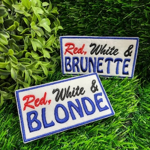 May include: Two rectangular embroidered patches with the text "Red, White & BRUNETTE" and "Red, White & BLONDE". The text is in red, white, and blue, with a white background and a blue border. The patches are on a green, grassy surface.
