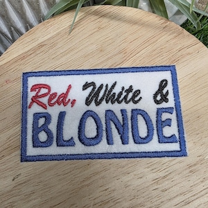 Pu&ograve; includere: Toppa ricamata con le parole "Red, White & BLONDE" in rosso, nero e blu. La toppa ha uno sfondo bianco con un bordo blu. Il testo &egrave; un mix di lettere corsive e a blocchi.