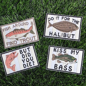 May include: Four embroidered patches with fishing-themed designs. One patch reads "Fish Around & Find Trout" with a red and brown fish. Another says "Do it for the Halibut" with a brown fish. A third says "But Did You Die?" with a red fish. The last says "Kiss My Bass" with a green fish.