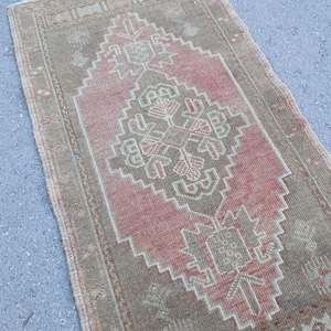 May include: A rectangular, vintage-style rug with a central pink diamond pattern and a border in shades of brown and green. The rug has a distressed look, with visible wear and tear.