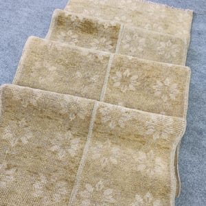 May include: A stack of beige and tan rugs with a floral pattern. The rugs are rectangular and have a slightly distressed appearance. The floral design is in a lighter shade, creating a subtle contrast.