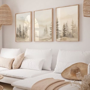 May include: A white sectional sofa with a light brown throw blanket and a straw hat on the couch. The sofa is in front of a white wall with three framed watercolour paintings of a foggy forest scene.