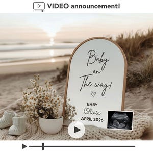 Peut inclure: Sc&egrave;ne d'annonce de grossesse sur une plage. Un panneau indique "B&eacute;b&eacute; en route !" avec le nom et la date d'accouchement du b&eacute;b&eacute;. La sc&egrave;ne comprend des chaussons de b&eacute;b&eacute;, un petit arrangement floral et une image d'&eacute;chographie. L'arri&egrave;re-plan montre l'oc&eacute;an et le coucher de soleil.