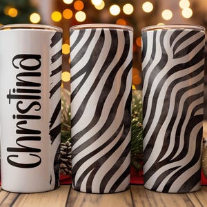 May include: Three stainless steel tumblers with a zebra print design. The tumbler on the left has the name "Christina" written on it in black.