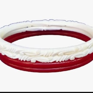 May include: A set of two stacked bangles consisting of one smooth, solid red bangle and one white bangle featuring a raised, carved leaf-like pattern along its outer surface. The bangles are circular and have a glossy, polished finish throughout.