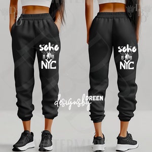 May include: Black sweatpants with a white graphic on the left leg that says "Soho NYC". The sweatpants have an elastic waistband and cuffs. The design includes a microphone, speakers, and a silhouette of people dancing.