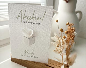 May include: A white card with the text "Abschied nehmen tut weh" and "Danke für die schöne Zeit!"  The card is propped up on a wooden stand with dried flowers.