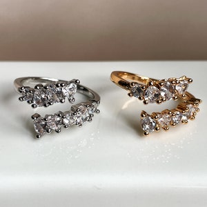 Può includere: Due anelli regolabili con una fila di pietre di zircone cubico trasparenti. L'anello a sinistra è d'argento e l'anello a destra è d'oro.