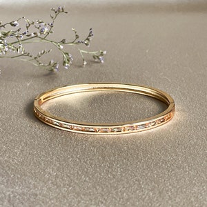 May include: A gold bangle bracelet with a row of clear rectangular stones around the edge.