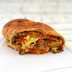 May include: A close-up of a breakfast casserole roll cut in half, revealing layers of scrambled eggs, sausage, peppers, and cheese inside a golden brown dough.
