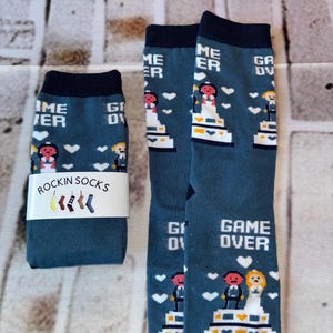 May include: A pair of blue socks with a white wedding cake design and the text "Game Over". The socks are a fun and unique gift for a couple getting married.