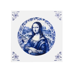 May include: A square ceramic tile featuring a blue and white depiction of the Mona Lisa. The artwork is framed by a floral border and set against a white background. Decorative floral corner accents complete the design.