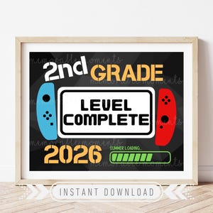 May include: Framed print with a black background featuring the words "2nd GRADE" and "LEVEL COMPLETE" in white and gold. Includes a blue and red game controller design and the year "2026". The bottom reads "SUMMER LOADING".