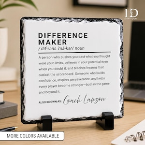 May include: A square slate plaque with a rough, dark gray chiseled edge and a smooth white center. The text reads: DIFFERENCE MAKER, followed by a phonetic pronunciation, a definition of the noun, and the personalized name Coach Lawson.