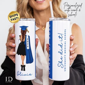 May include: Two white insulated tumblers with blue and black graphics. One features a graduation illustration with the name "Olivia" and the year "2026." The other says "She did it!" and "University Medical School."