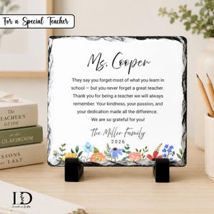 May include: A square slate plaque with rough, dark edges, displayed on two black stands. The white center features black text: Ms. Cooper, a thank you message, The Miller Family, and 2026, accented by a colorful watercolor floral border at the bottom.