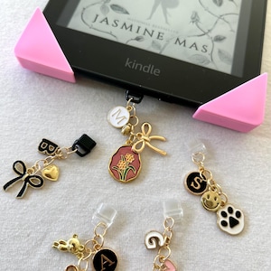 May include: Five gold-toned bookmark charms with different designs. The charms include a black letter A, a black letter S, a black letter M, a pink flower with a gold center, and a pink bear with a gold heart. The charms are attached to clear plastic clips.