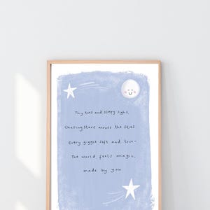 May include: A framed art print with a light wood frame. The artwork features a light blue background with a moon and stars illustration. The text reads: "Tiny toes and sleepy sighs, Chasing stars across the skies. Every giggle soft and true- The world feels magic, made by you."