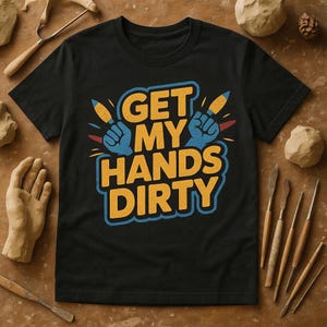May include: Black t-shirt with the phrase "GET MY HANDS DIRTY" in yellow and blue. The design includes blue hands holding yellow tools. The shirt is surrounded by clay sculpting tools and clay.
