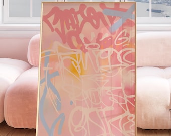 May include: Abstract art print with a gold frame. The artwork features a blend of pink, white, yellow, and blue graffiti-style markings on a soft pink background. The piece is displayed in a room with a pink sofa and a window overlooking a cityscape.