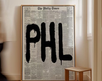 May include: Framed artwork featuring a vintage newspaper background with the word "PHL" in large, dripping black letters. The text "The Philly Times" is printed at the top. A small wooden stool sits nearby.