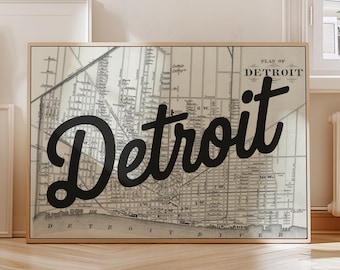 May include: Framed vintage map of Detroit with the city name in a bold, black script overlaying the map. The map is in grayscale, with a gold-colored frame. The words "Plan of Detroit" are above the city name.