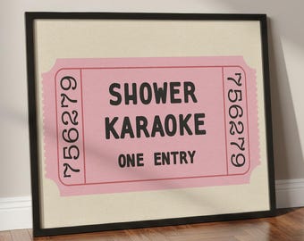 May include: A framed pink ticket with the words "Shower Karaoke One Entry" in black. The ticket has a serrated edge and the number 756279 printed on both sides. The frame is black.