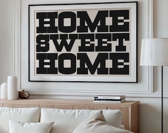 May include: A framed black and white art print with the words "HOME SWEET HOME" in bold, block letters. The print hangs above a light wood cabinet and a white sofa with beige pillows. A floor lamp stands to the right.