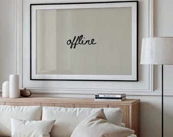 May include: A living room scene featuring a cream-colored sofa with several pillows, a wooden coffee table, and a wooden cabinet. A large framed print with the word "offline" in cursive is mounted above the cabinet. A floor lamp with a white shade stands to the right.