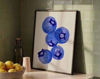 May include: A framed watercolor print featuring a cluster of six blue blueberries. The blueberries have a dark blue outline and a lighter blue interior. The print is displayed on a kitchen counter with lemons in a wooden bowl.