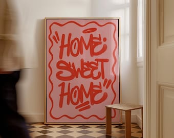 May include: A framed pink art print with the words "HOME SWEET HOME" in red graffiti-style lettering. The artwork is displayed in a room with a checkered floor and a small wooden side table.