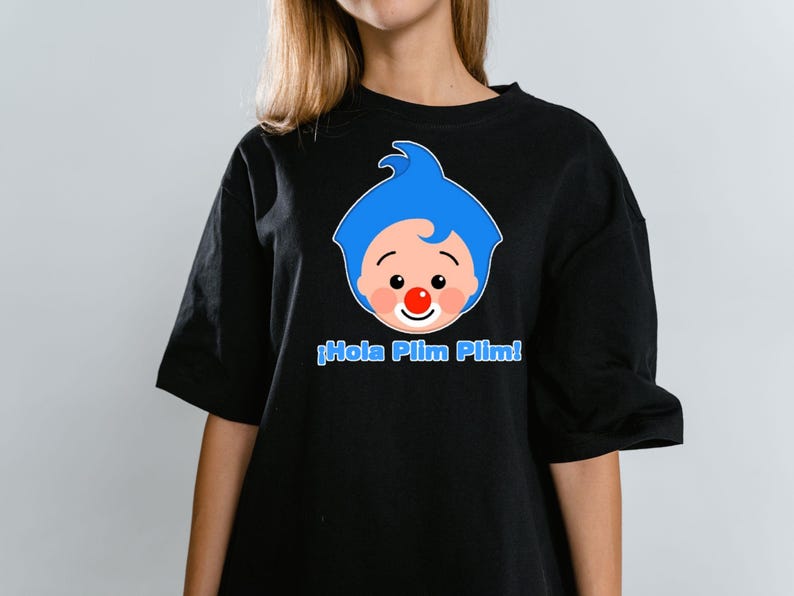 May include: Black t-shirt featuring a cartoon clown face with blue hair, a red nose, and the text "&iexcl;Hola Plim Plim!" in blue. The shirt is a casual style, suitable for everyday wear.