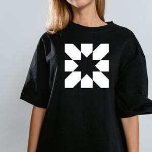 May include: Black t-shirt featuring a white geometric starburst design. The graphic is centered on the chest. The shirt has short sleeves and a crew neck. The fabric appears to be a soft cotton blend.