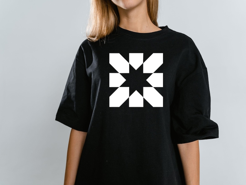 May include: Black t-shirt featuring a white geometric starburst design. The graphic is centered on the chest. The shirt has short sleeves and a crew neck. The fabric appears to be a soft cotton blend.