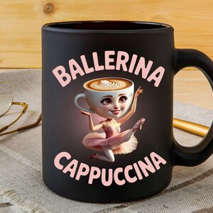 Może przedstawiać: Czarny ceramiczny kubek z r&oacute;żowymi napisami "Ballerina Cappuccina". Kubek przedstawia kresk&oacute;wkową baletnicę z filiżanką kawy zamiast głowy. Baletnica ma na sobie r&oacute;żowe tutu i jest w pozie baletowej.