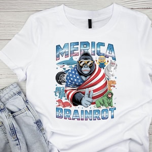 Może przedstawiać: Biała koszulka z gorylem w okularach przeciwsłonecznych i amerykańską flagą, z napisem "MERICA" powyżej i "BRAINROT" poniżej. Zawiera kresk&oacute;wkowe obrazy rekina, Minionka, kota, dinozaura i innych.