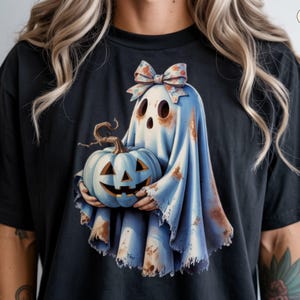 Op de afbeelding: Zwart T-shirt met een Halloween-thema. Het ontwerp toont een geest met een strik en een blauwe pompoen met een uitgesneden gezicht. De tekst "ClassyAs Name" staat rechtsboven. Een griezelig en leuk ontwerp.