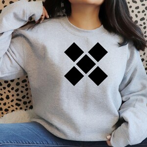 May include: A light gray sweatshirt featuring a black geometric design of five connected diamonds. The sweatshirt has a crew neck and long sleeves. The background is a spotted pattern.