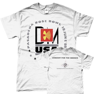 May include: White t-shirt featuring a black and red graphic of the letters "DM" with a sound wave inside the "M". The graphic is surrounded by the text "PASADENA ROSE BOWL 18 JUN E'88" and "USA". The back of the shirt has the text "CONCERT FOR THE MASSES" and a graphic of a globe with a sound wave around it. The text "Spreading the News around the World" is below the globe.